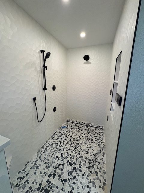 Modern bathroom renovation showcasing unique textured walls and stylish pebble flooring done in Punta Gorda.